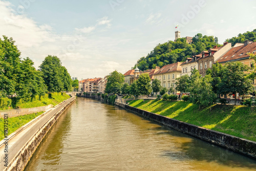 Sunny view of a European city with historical buildings lining the banks of Ljubljana river, overlooked by a hilltop castle, Ljubljana, Slovenia photo