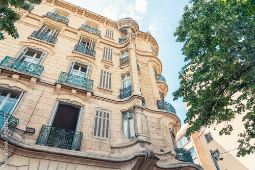 Elegant Parisian  or provencial building with wrought iron balconies under a clear blue sky, flanked by green trees, Marseille, France photo