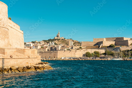 Coastal view of a historical fort of Saint Jean and Citadel of Marseille and city with a Basilica of Notre Dame de la Garde, on a hill under a clear blue sky, Marseille, France
