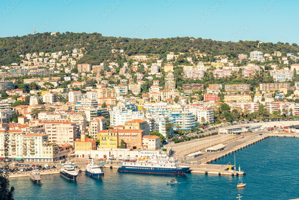 Scenic view of a coastal town with colorful buildings, a bustling Nice Port, and hillside homes under a clear blue sky, Nice, France Scenic view of a coastal town with colorful buildings, a bustling Nice Port, and hillside homes under a clear blue sky, Nice, France