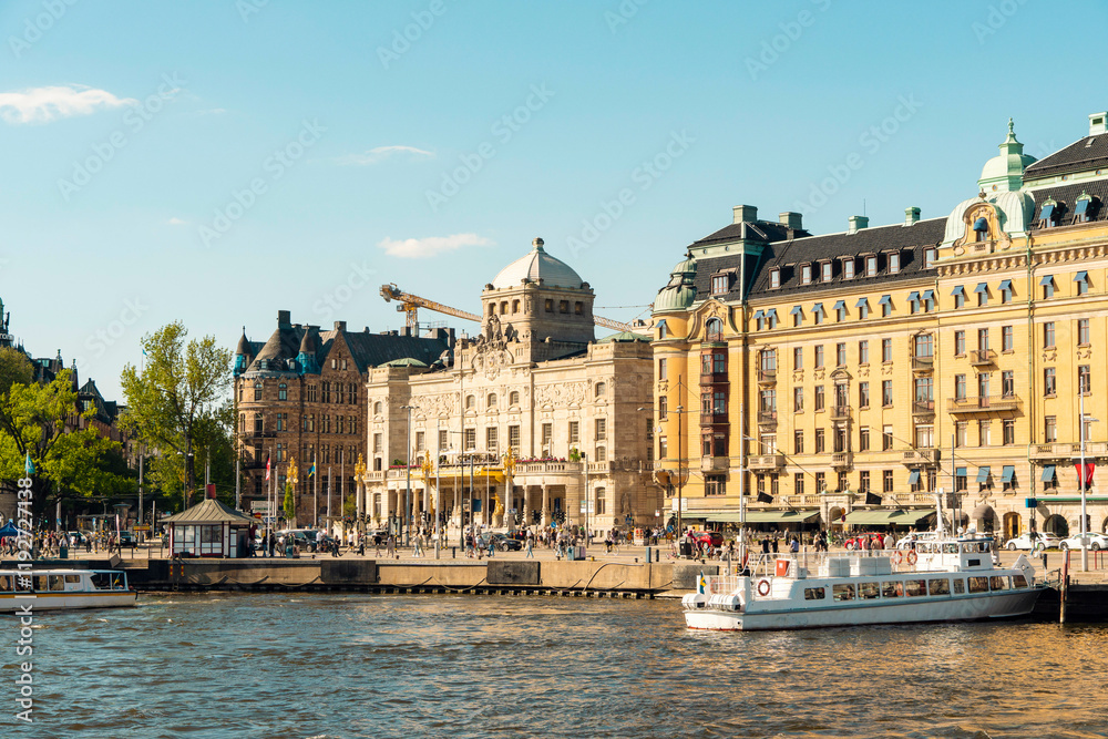 Sunny day view of a bustling waterfront with classic architecture and The Royal Dramatic Theater and sightseeing boats in Stockholm, Sweden Sunny day view of a bustling waterfront with classic architecture and The Royal Dramatic Theater and sightseeing boats in Stockholm, Sweden