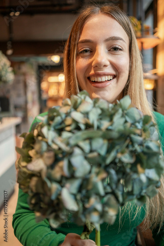 Smiling young woman holding a bouquet of green leaves stands inside a brightly lit store, Berlin, Germany photo