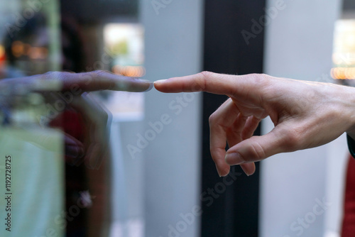 Close-up of a person's hand reaching out to touch a glass surface with a reflection visible, Berlin, Germany photo