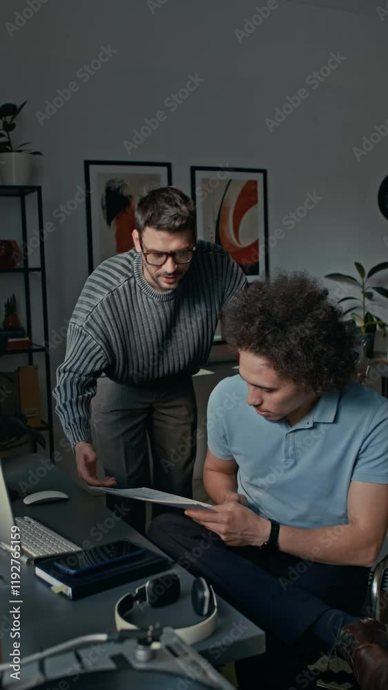 Vertical shot of man in glasses asking his colleague with curly hair for help with documents in modern open space office Vertical shot of man in glasses asking his colleague with curly hair for help with documents in modern open space office