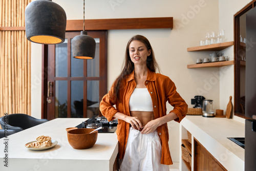 Young woman in a stylish kitchen preparing healthy food while wearing an orange shirt and white pants conveying a sense of wellness and lifestyle photo