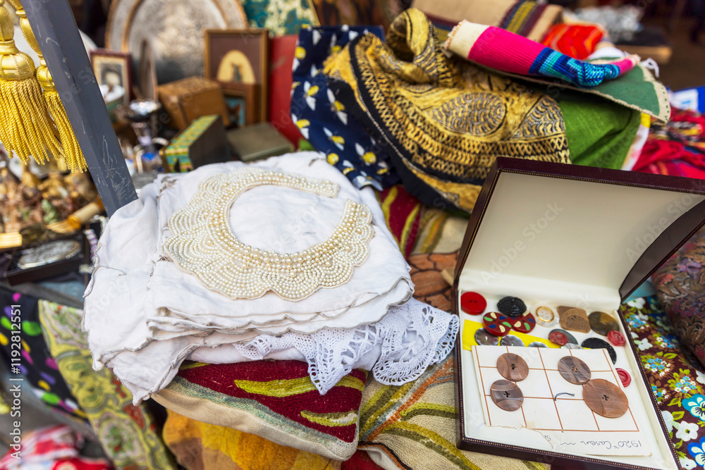 Naklejka premium Vintage embroidery, pearl necklace, buttons in a box, and silk scarves for sale at a flea market.