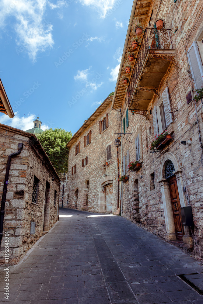 Medieval architecture and narrow streets of Assisi, traditional stone houses with balconies and a charming vintage scooter hidden in the distance.