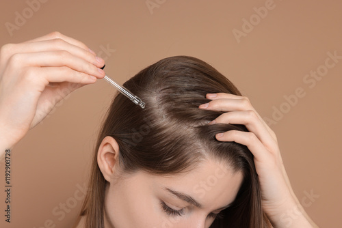 Hair loss problem. Girl applying serum onto hairline on dark beige background, closeup