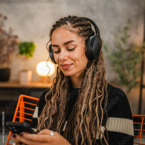 young woman with headphones use mobile phone and enjoy on armchair