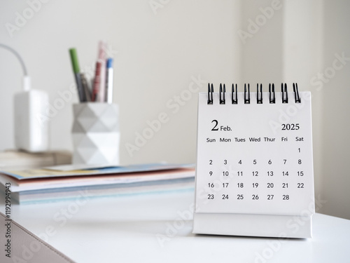 A February 2025 calendar desk for the organizer to plan and reminder standing on white desk in working room at home. White small table calendar with the page of the second month, Happy new year 2025. photo