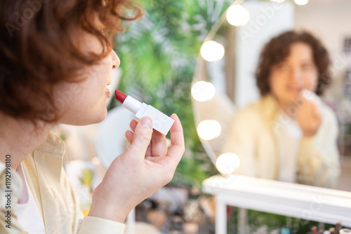 Person applying organic red lipstick in front of a vanity mirror photo