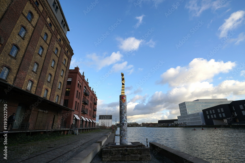 Fototapeta premium Alter Getreidespeicher und Lagerhaus aus rotbraunem Backstein mit Statue auf einer Säule vor blauem Himmel mit weißen Wolken am Kreativkai am alten Hafen von Münster in Westfalen im Münsterland