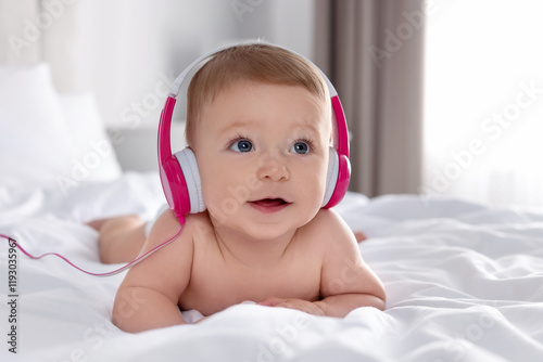 Cute little baby with headphones on bed at home photo