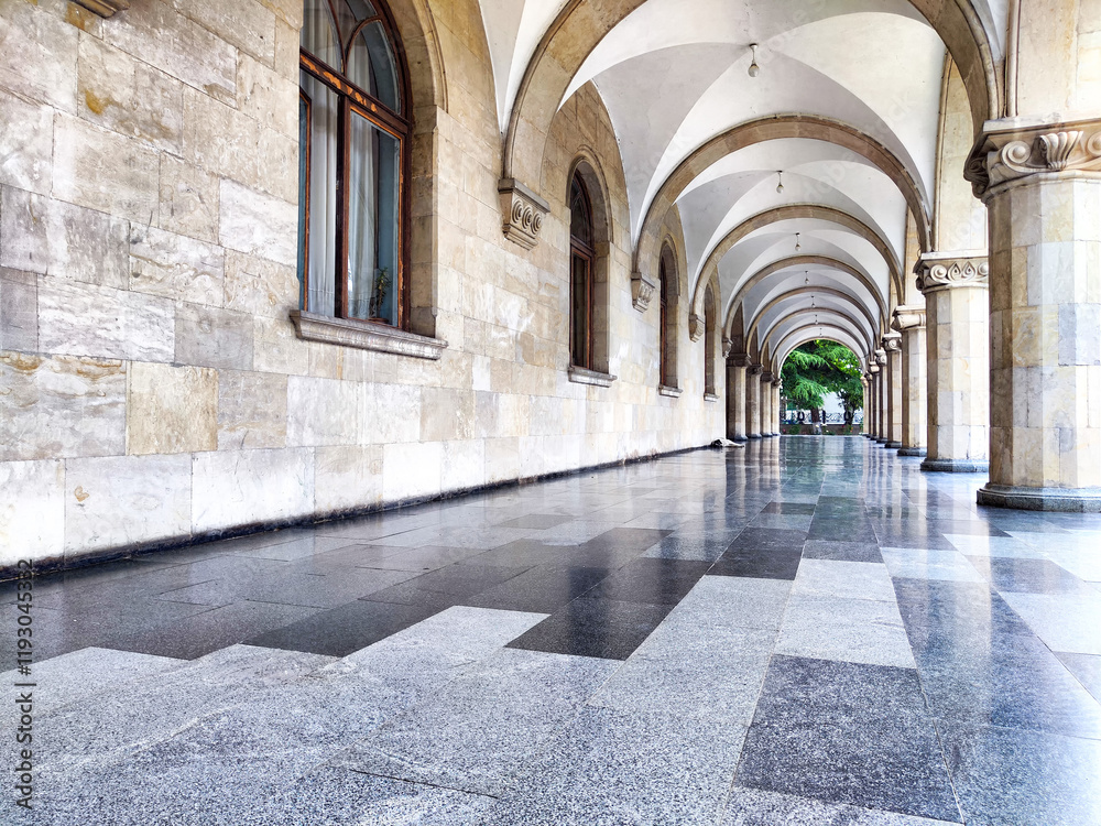 Obraz premium Historic architectural beauty featuring arched corridors and polished stone floors in a quiet urban setting