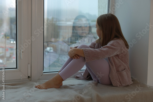 Autism concept. Lonely little girl near window at home photo