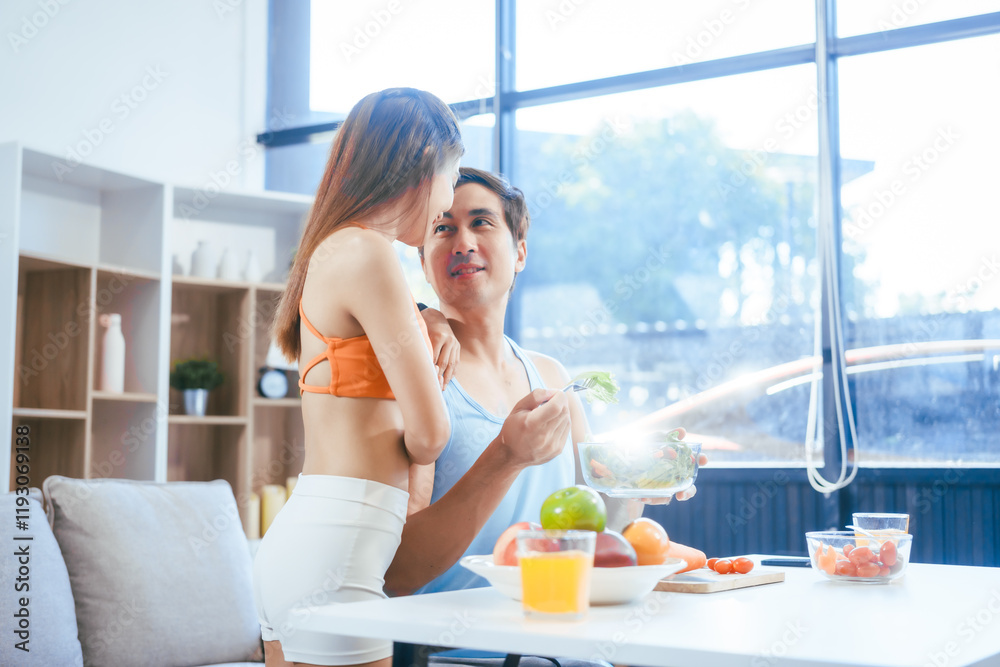 A happy young couple in sportswear sits on the sofa after exercising, enjoying fruits, salad, and orange juice. They focus on weight loss, weight control, and living a healthy lifestyle A happy young couple in sportswear sits on the sofa after exercising, enjoying fruits, salad, and orange juice. They focus on weight loss, weight control, and living a healthy lifestyle