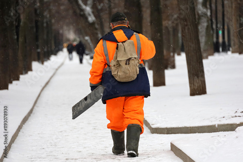 Communal services worker in uniform with a shovel walking by snow in winter park, street cleaning in city photo