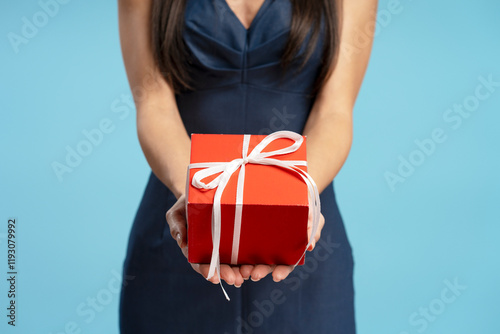 Woman holding red gift box with white ribbon on blue background
