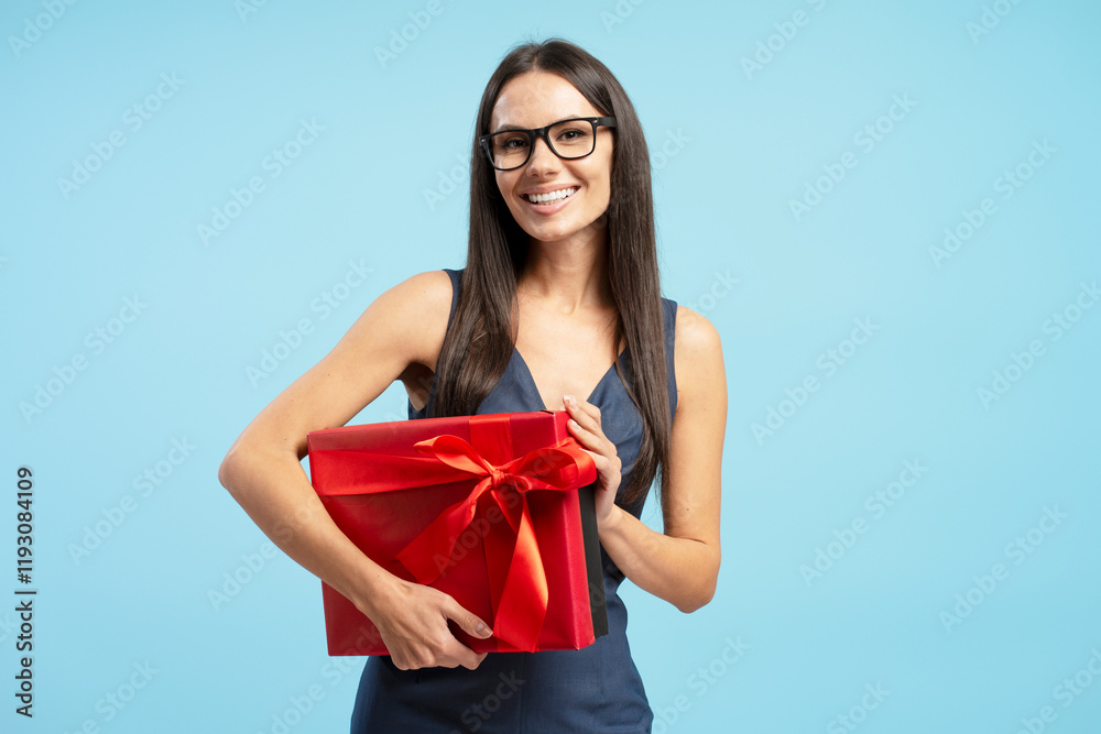 Happy Hispanic woman wearing eyeglasses holding a red gift box with ribbon on blue background Happy Hispanic woman wearing eyeglasses holding a red gift box with ribbon on blue background