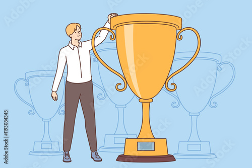 Man business leader stands near giant golden cup symbolizing award for best employee