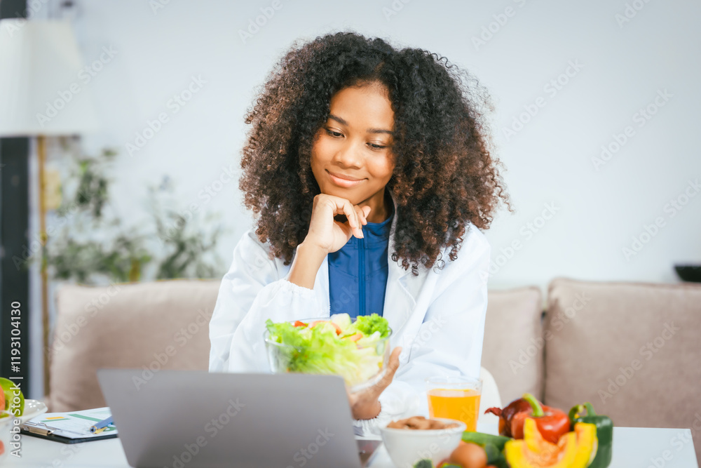 An African American female nutritionist sits at a table, consulting online with patients. She talks about the benefits of eating fruits and vegetables, emphasizing healthy eating and the importance An African American female nutritionist sits at a table, consulting online with patients. She talks about the benefits of eating fruits and vegetables, emphasizing healthy eating and the importance