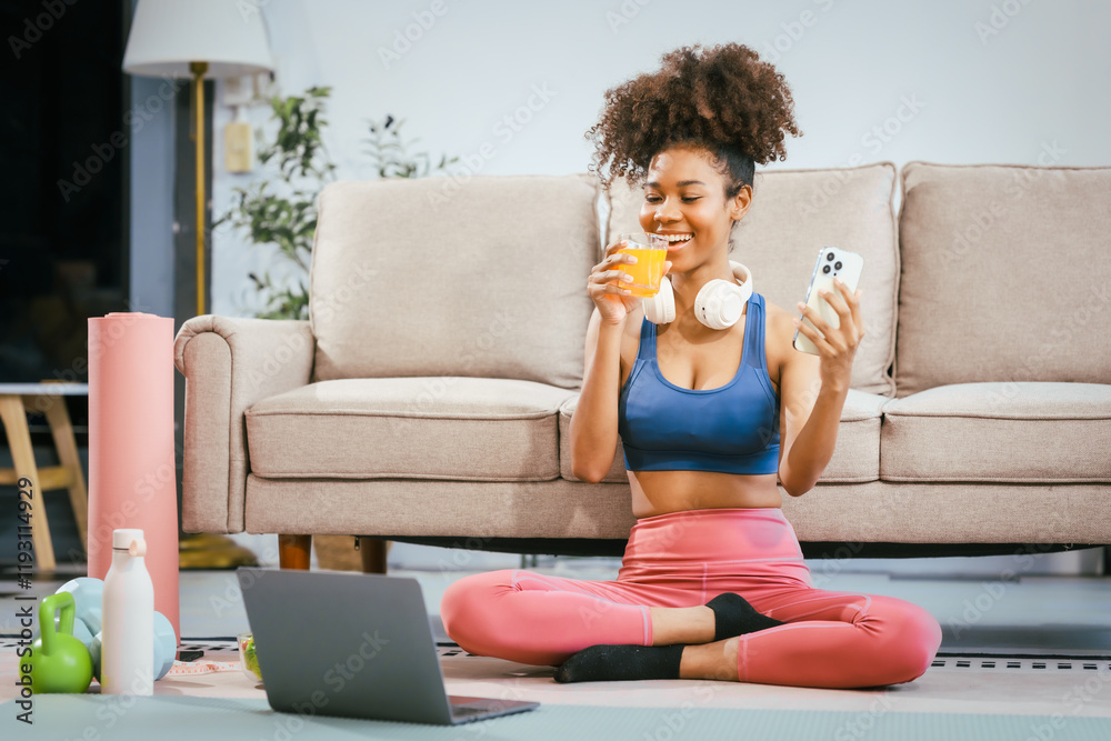 An African American woman in workout clothes and headphones enjoys a fresh salad and orange juice at home after a hard workout. She uses her computer, focusing on health care and daily exercise An African American woman in workout clothes and headphones enjoys a fresh salad and orange juice at home after a hard workout. She uses her computer, focusing on health care and daily exercise