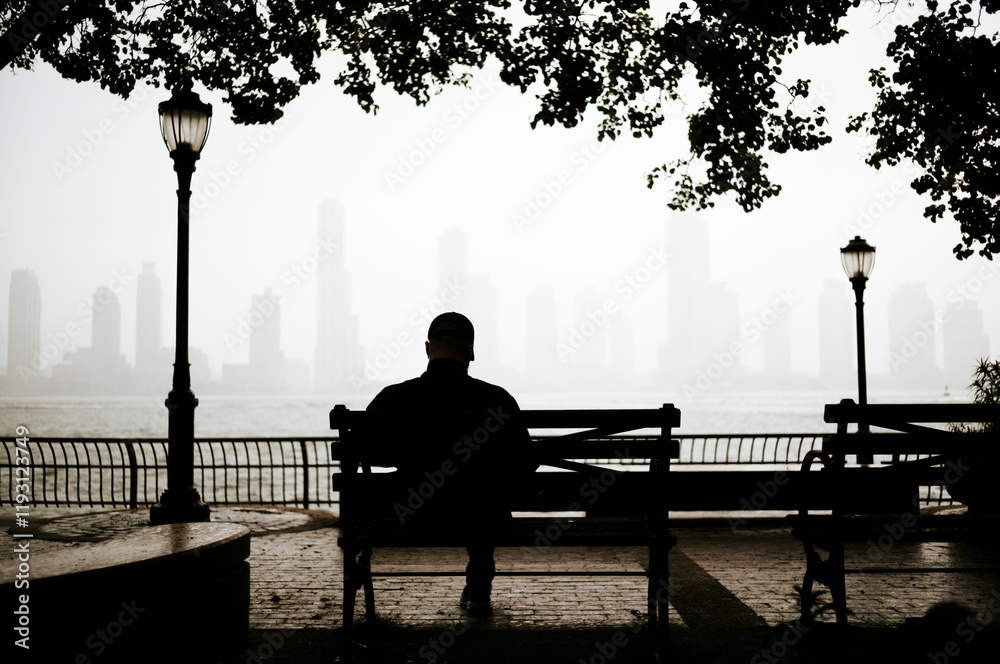 Silhuete of a man sitting on a bench with view of Manhattan city in the background, New York, USA