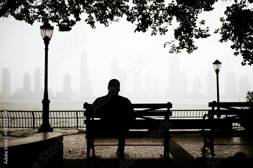 Obraz na płótnie Silhuete of a man sitting on a bench with view of Manhattan city in the background, New York, USA w salonie