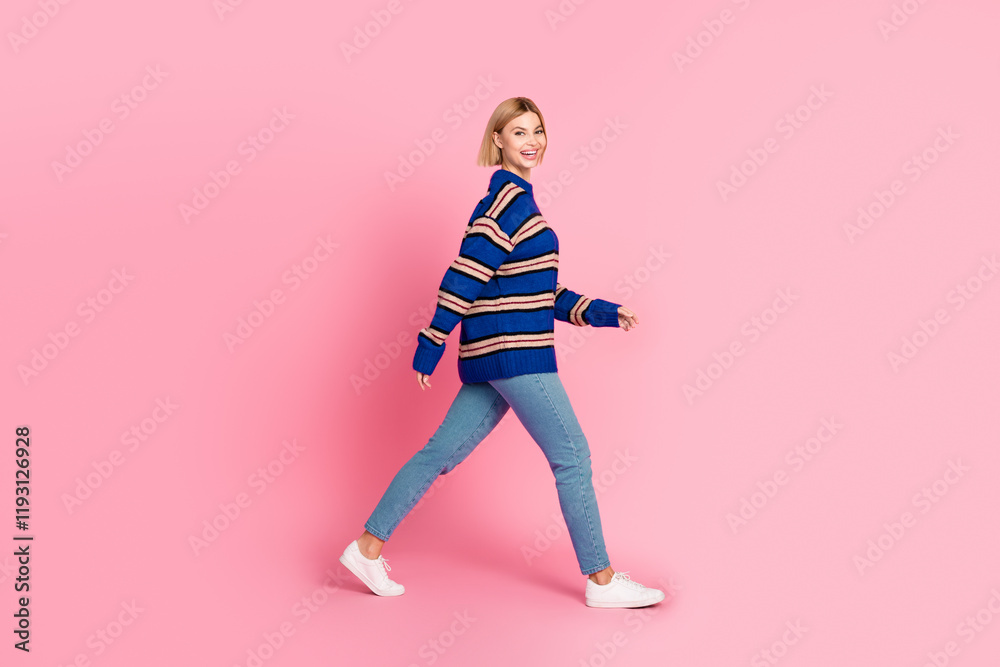 Smiling woman walking joyfully on pink background wearing stylish striped sweater and denim jeans Smiling woman walking joyfully on pink background wearing stylish striped sweater and denim jeans