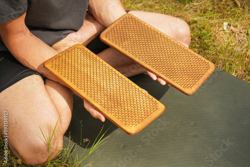 Close-up of a man's hands holding a sadhu board in his hands with nails pointing up. Outdoors, a man on a yoga mat is about to perform exercises. photo