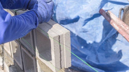 A male worker uses his hands to pound vent bricks to make them level along lines stretched with tendons. A bricklayer works on a construction site. photo