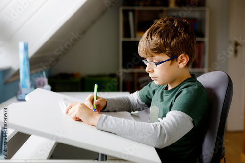 Kid boy with glasses learns at home for school. Preteen child making homework.