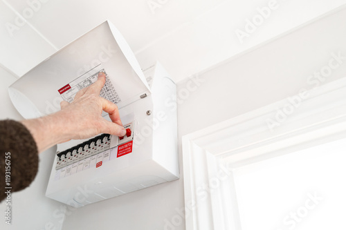 Electrician seen about to switch off the Main Switch for electricity into a typical house. Circuit breakers can be seen for various electrical areas with a typical house.