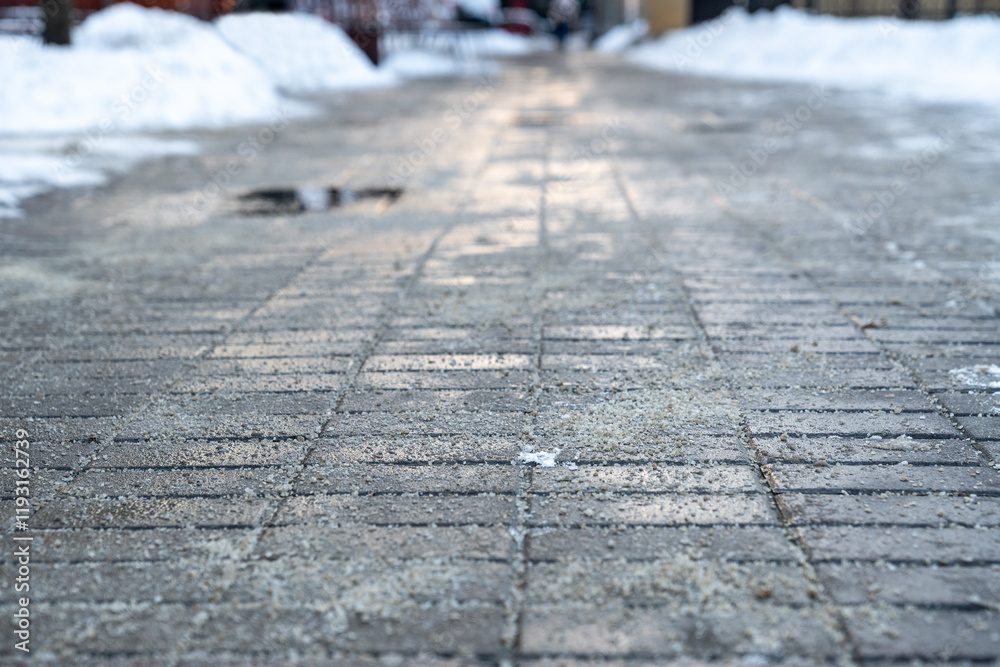 Fototapeta premium Road surface treated with technical salt to prevent ice formation, salt puddles on the road. Snow removal and maintenance of footpaths in winter time