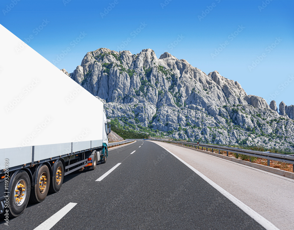 A white truck transports cargo along the highway against the backdrop of a mountain landscape.