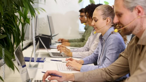 Customer service representative working in busy modern office using laptop and headset