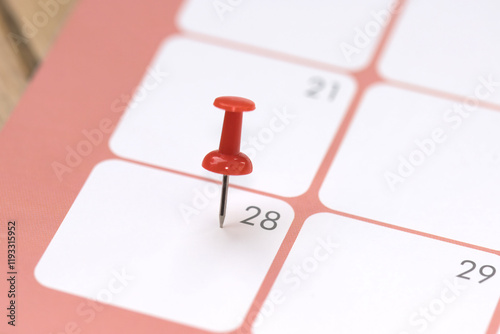 Calendar entry: Number 28 pinned with a red push pin or thumbtack, symbolizing the “Save the Date” concept. photo