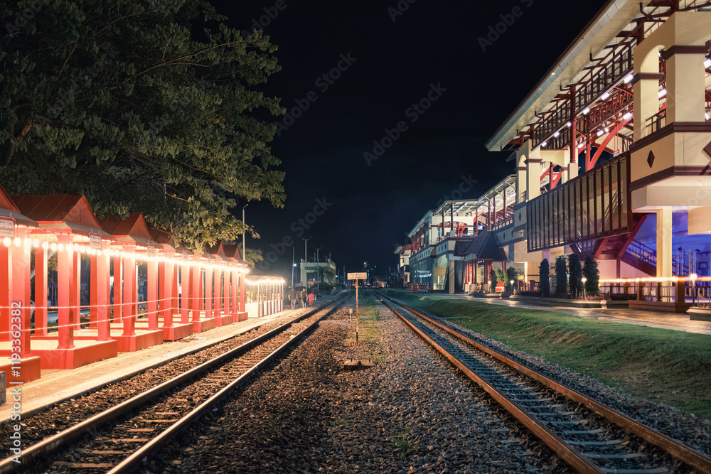 Fototapeta premium Illuminated large building of train station with railway platform in the night