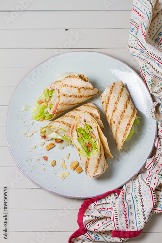 Chicken bacon caeser wrap. Chicken breast fillet wraps on green plate on light wooden background. View from above, top view