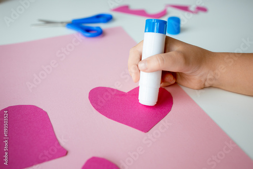 Child crafting heart shapes with pink paper and glue stick