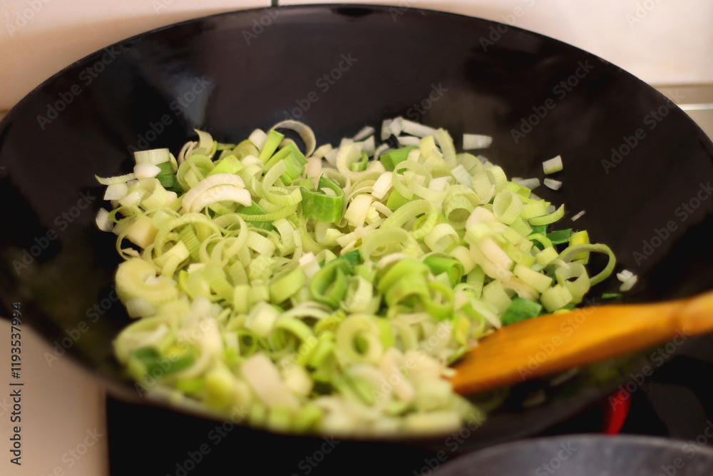 Sauteing chopped leek slices in a wok. Selective focus.