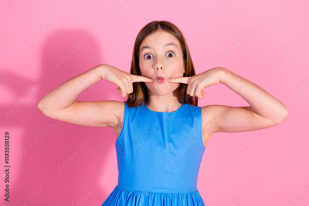 Charming young girl with a playful expression in a blue dress against a pink background Charming young girl with a playful expression in a blue dress against a pink background