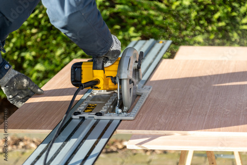 Male using electric circular saw to cut DIY sheet material outside