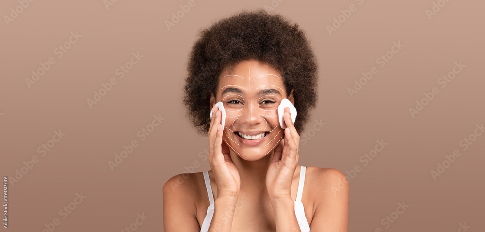 African American woman enjoys her skincare routine, applying cleanser on her face with cotton pads. She is isolated against a solid background, radiating joy during her pampering session. African American woman enjoys her skincare routine, applying cleanser on her face with cotton pads. She is isolated against a solid background, radiating joy during her pampering session.