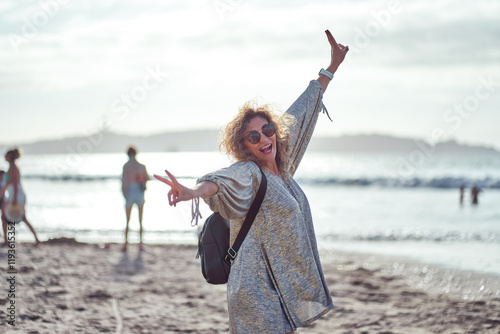 Carefree mature woman enjoying freedom on sandy beach, showing peace sign with ocean waves in background in La Serena, Coquimbo region photo