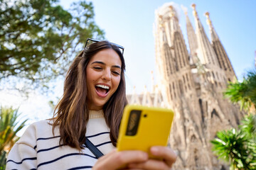 Young women friend using mobile phone in hands in front of Sagrada Familia in Barcelona. Beautiful caucasian girls at European city enjoying vacation happy and smiling. Funny tourism smile people