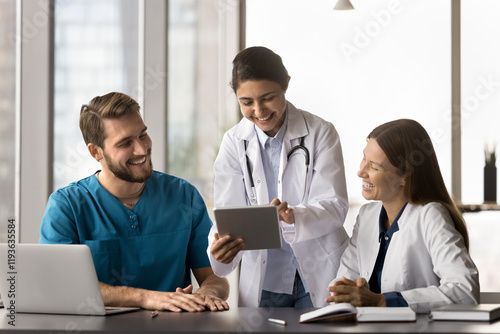 Three multiethnic medical worker using modern digital tablet device at workplace, sharing humorous, positive moment at break, read good news related to patient progress or successful treatment outcome photo