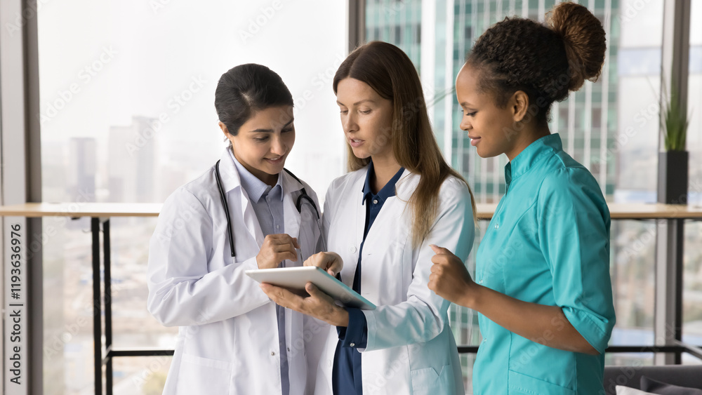 Nurses and GP dressed in uniforms standing in clinic office, talking, using tablet at workplace. Review latest updates, learn new platform, telemedicine application, share opinion regarding treatment Nurses and GP dressed in uniforms standing in clinic office, talking, using tablet at workplace. Review latest updates, learn new platform, telemedicine application, share opinion regarding treatment