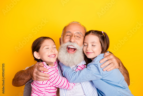 Grandfather joyfully hugging two young granddaughters on a bright yellow background with happy, loving expressions.