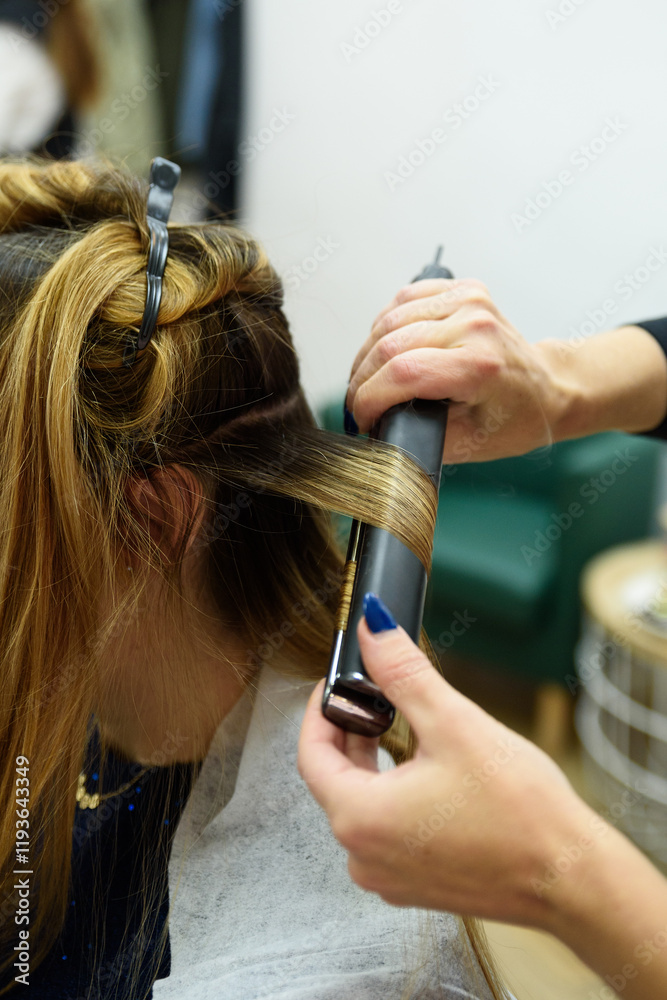 Fototapeta premium Hairdresser straightening woman's hair with hair straightener in salon